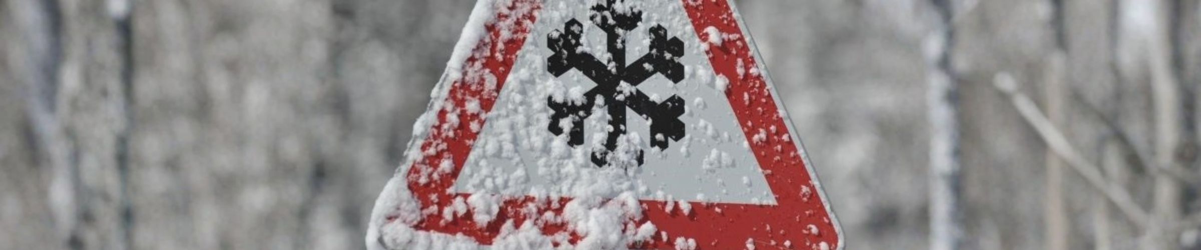 Verkeersbord met een sneeuwvlok als waarschuwing voor gladheid, bedekt met sneeuw in een winterse omgeving.