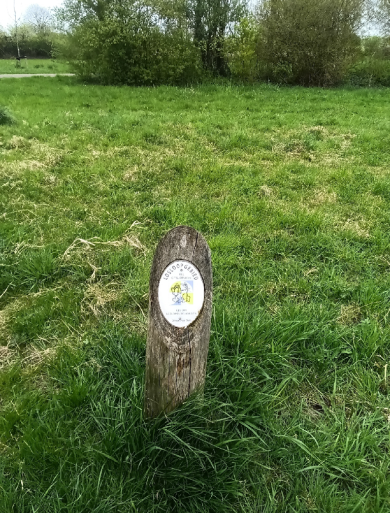 houten paaltje op grasveld met daarop een wit bordje waar losloopgebied op staat