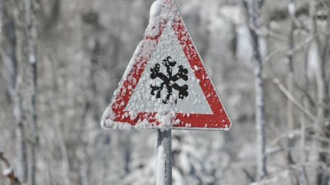 Verkeersbord met een sneeuwvlok als waarschuwing voor gladheid, bedekt met sneeuw in een winterse omgeving.