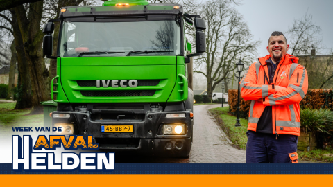 Afvalinzamelaar in oranje werkkleding staat naast een groene Avri-vrachtwagen op een woonstraat, met de tekst “Week van de AfvalHelden” in beeld.